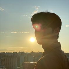 a man standing in front of the sun on top of a building with buildings behind him