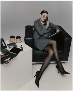 a woman is sitting on a chair with her legs crossed and holding a book in one hand