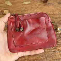 a hand holding a red leather wallet on top of a wooden table next to nuts