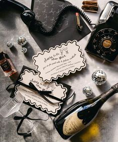 an assortment of personal items on top of a silver table cloth with a phone, wine bottle and glasses