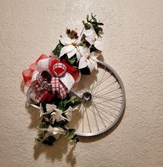 a bicycle wheel decorated with flowers and ribbon on the wall in front of a stucco wall