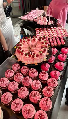 a table topped with lots of cupcakes covered in pink frosting