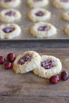 two cookies with jam on them are sitting on a baking sheet next to some cranberries