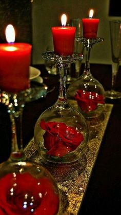 three wine glasses with red roses in them are sitting on a table next to candles