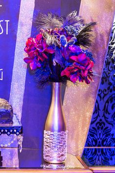 a vase filled with purple and red flowers on top of a table next to a cake