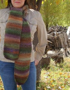 a woman is standing in the grass wearing a multicolored crocheted scarf