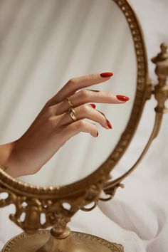 a woman's hand with red nail polish is reflected in a gold circular mirror