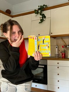 a woman holding up a yellow book in the kitchen