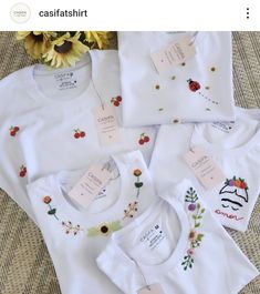 four white t - shirts with embroidered flowers and ladybugs on them are sitting next to each other