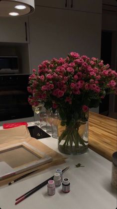 a vase filled with pink flowers sitting on top of a table next to paint and brushes