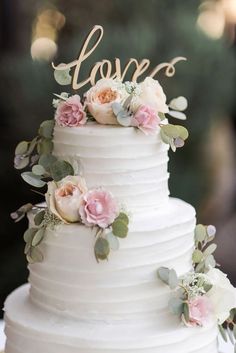 a white wedding cake with pink flowers and the word love written on top is sitting on a table