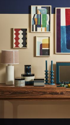 a wooden table topped with lots of art on top of a wall next to a lamp