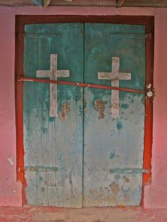 two wooden doors with crosses on them in an old building that has been painted pink and blue