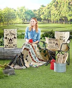 a woman sitting on top of a chair next to a fire pit and camping gear