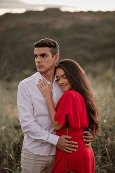 a man and woman standing together in the middle of a field with tall grass at sunset