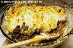 a casserole dish with meat, cheese and vegetables is being held by a wooden spoon