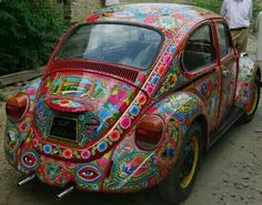 a colorfully painted beetle parked on the side of a road with people standing next to it