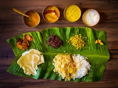 a banana leaf with different types of food on it, including rice and sauces