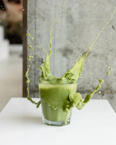 a glass filled with green liquid sitting on top of a white table next to a wall