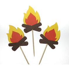 three sticks with paper cut out of fire and flames on them, sitting in front of a white wall