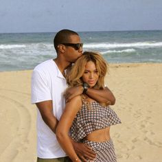 a man standing next to a woman on top of a sandy beach near the ocean