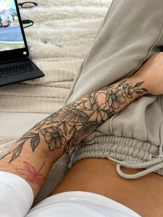 a person with a flower tattoo on their arm and leg sitting in front of a laptop