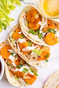 three tacos with chicken and lettuce next to dipping sauce on the side