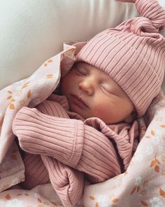 a newborn baby wrapped in a blanket and wearing a pink hat is sleeping on a bed