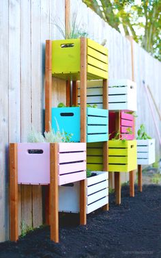 colorful crates are lined up against a wooden fence with plants growing out of them,