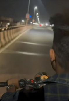 the man is driving his motorcycle down the road at night with street lights in the background