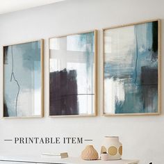 three paintings hang on the wall above a white table with vases and two lamps