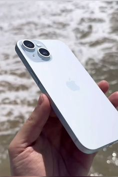 a person holding an iphone in their hand near the water and waves on the beach