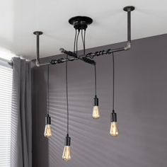 three light fixtures hanging from the ceiling in a room with grey walls and curtains behind them