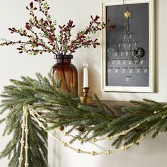 a decorated mantle with candles and greenery on it, next to a framed calendar