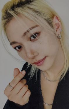 a young woman with blonde hair wearing a black jacket and silver necklace, posing for the camera