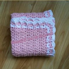 a pink and white crocheted blanket sitting on top of a wooden floor