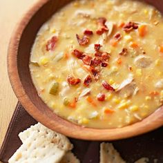 a wooden bowl filled with soup next to crackers on top of a brown table