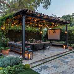 an outdoor patio with seating and lights on the ceiling, surrounded by greenery at dusk