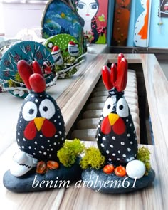 two rooster statues sitting on top of a wooden table next to each other in the shape of eggs