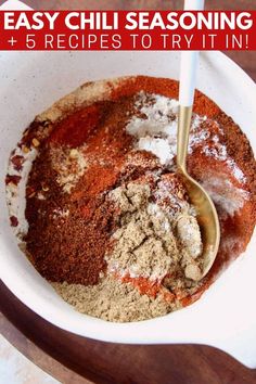 a bowl filled with spices and seasoning on top of a wooden table next to a spoon