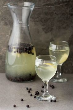 two glasses and a pitcher filled with liquid on a gray surface next to some blackberries