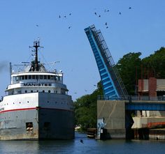 a large boat in the water next to a bridge and some birds flying over it