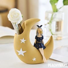 a figurine sitting on the moon next to a pen holder