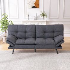 a gray couch sitting on top of a wooden floor next to a white rug and potted plant