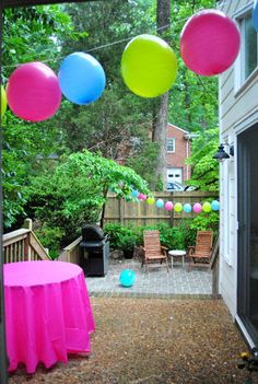 balloons are hanging from the ceiling in front of a patio with pink and green tablecloths