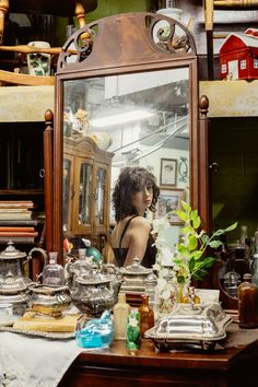 a woman standing in front of a mirror next to a table with dishes on it