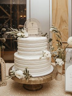 a white wedding cake sitting on top of a wooden stand next to flowers and greenery