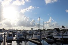 many boats are docked in the water under a cloudy blue sky with sunbeams