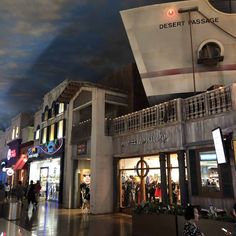 people are walking around in front of the desert passage store at night with clouds painted on the ceiling