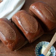 three loaves of bread sitting on top of a wooden table next to a bowl